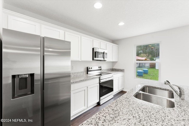 kitchen with white cabinets, sink, dark hardwood / wood-style floors, light stone countertops, and appliances with stainless steel finishes