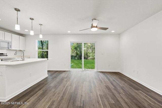 unfurnished living room featuring ceiling fan, a healthy amount of sunlight, sink, and dark hardwood / wood-style flooring