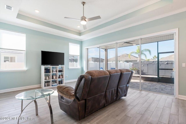 living room with a healthy amount of sunlight, a raised ceiling, light hardwood / wood-style floors, and crown molding