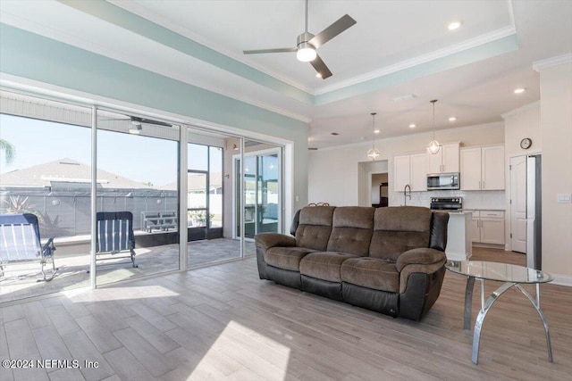 living room featuring a tray ceiling, crown molding, ceiling fan, and light wood-type flooring