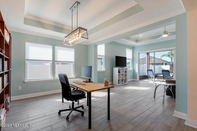 office featuring a tray ceiling, ceiling fan, ornamental molding, and light wood-type flooring