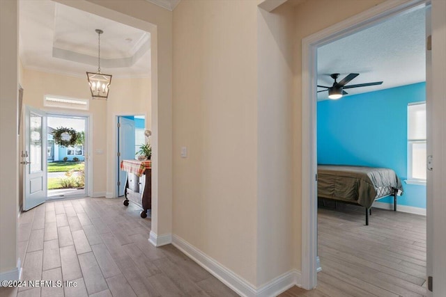 hallway with a tray ceiling, ornamental molding, a notable chandelier, and light wood-type flooring