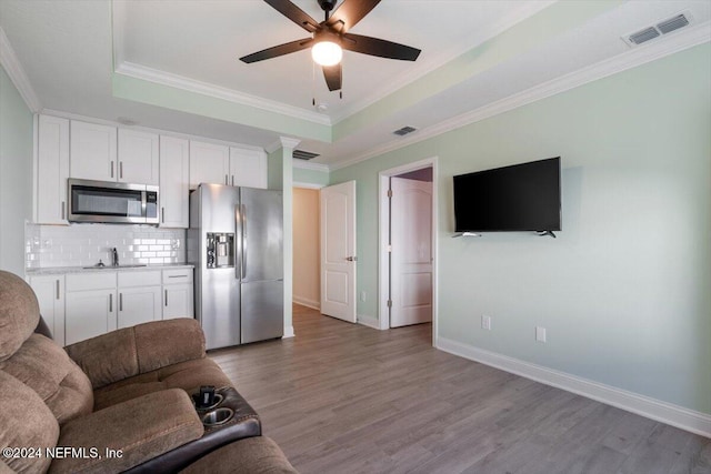 living room featuring a raised ceiling, ceiling fan, wood-type flooring, and ornamental molding