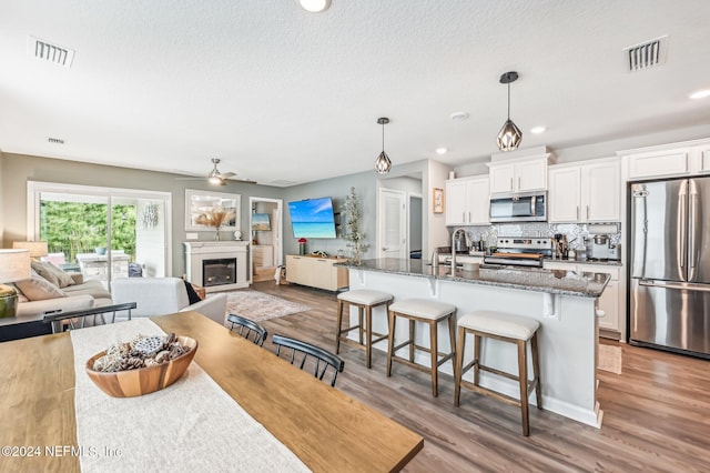 kitchen with stainless steel appliances, white cabinetry, a center island with sink, a breakfast bar, and dark stone counters