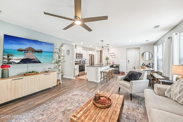 living room with ceiling fan, a textured ceiling, sink, and light wood-type flooring