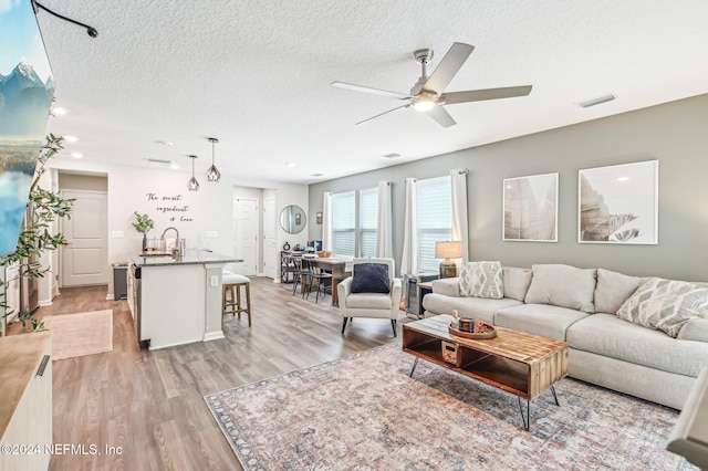 living room with sink, light wood-type flooring, a textured ceiling, and ceiling fan