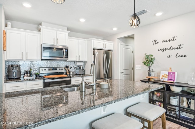 kitchen featuring stainless steel appliances, light hardwood / wood-style floors, dark stone countertops, hanging light fixtures, and white cabinets