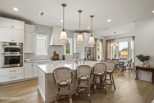 55A Solana Rd, Ponte Vedra Beach, FL 32082 - kitchen with appliances with stainless steel finishes, custom exhaust hood, an island with sink, decorative backsplash, and light wood-style flooring