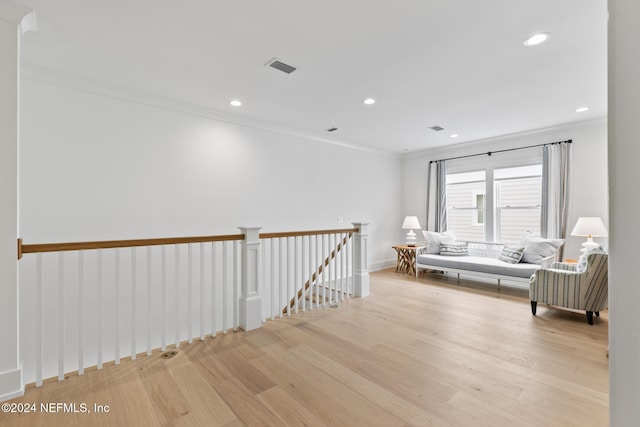 unfurnished room with light wood-type flooring, visible vents, ornamental molding, and an upstairs landing