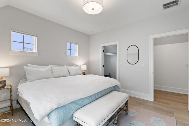 bedroom with lofted ceiling, light wood-style flooring, visible vents, baseboards, and a spacious closet