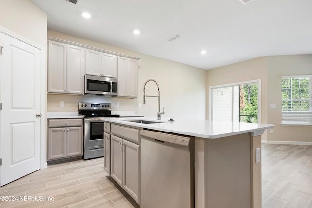 kitchen with sink, appliances with stainless steel finishes, a kitchen island with sink, light hardwood / wood-style flooring, and gray cabinets