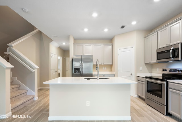 kitchen with appliances with stainless steel finishes, sink, an island with sink, and light hardwood / wood-style floors