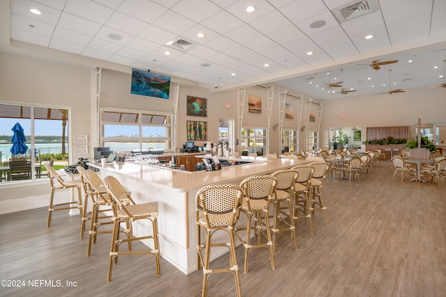 kitchen with a kitchen breakfast bar, a towering ceiling, ceiling fan, and light hardwood / wood-style floors