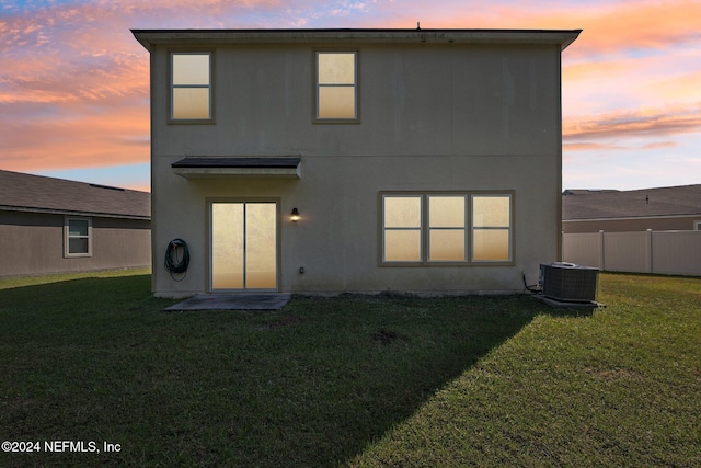 back house at dusk with a yard and central AC unit