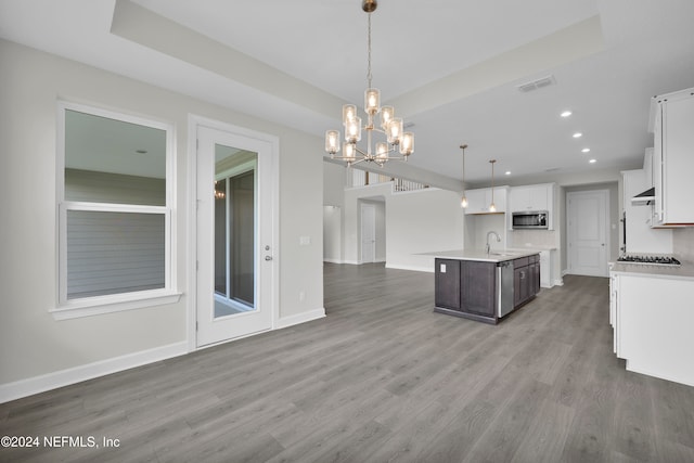 kitchen featuring white cabinets, hardwood / wood-style floors, a chandelier, a kitchen island with sink, and decorative light fixtures