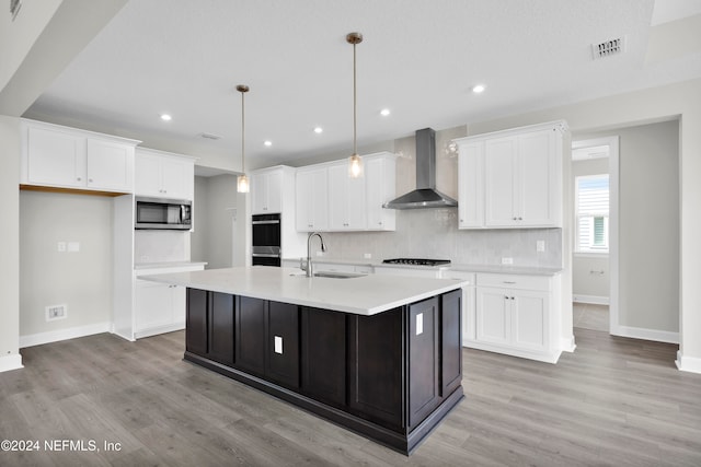 kitchen featuring stainless steel appliances, sink, decorative light fixtures, a kitchen island with sink, and wall chimney range hood