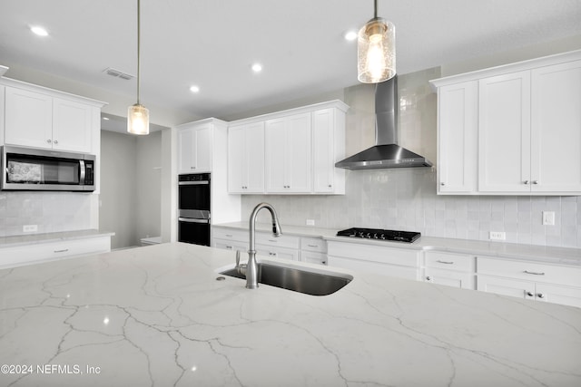 kitchen featuring sink, appliances with stainless steel finishes, wall chimney exhaust hood, white cabinets, and pendant lighting