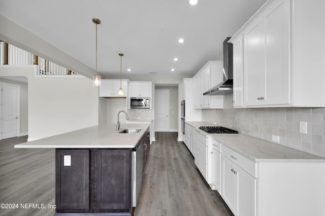 kitchen with appliances with stainless steel finishes, decorative light fixtures, sink, wall chimney exhaust hood, and light hardwood / wood-style flooring