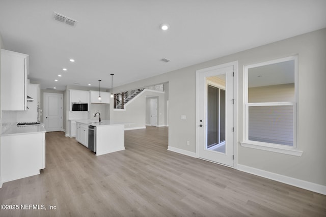 kitchen featuring a sink, visible vents, light countertops, stainless steel dishwasher, and light wood finished floors