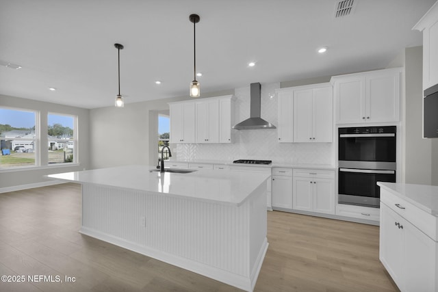 kitchen with wall chimney exhaust hood, double oven, a sink, and light wood-style flooring