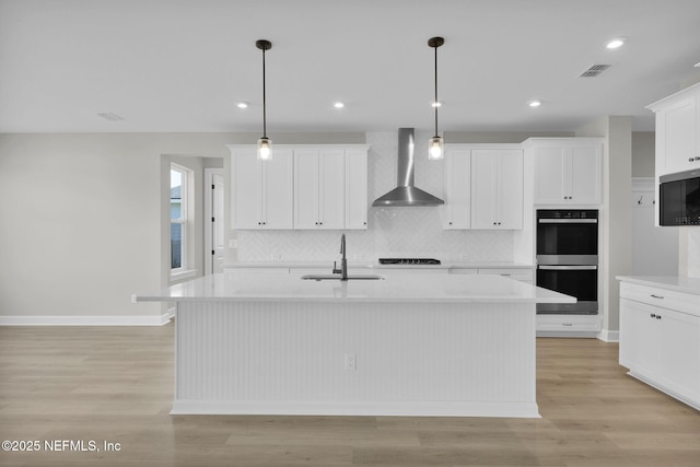 kitchen featuring stainless steel double oven, a sink, visible vents, light countertops, and wall chimney range hood