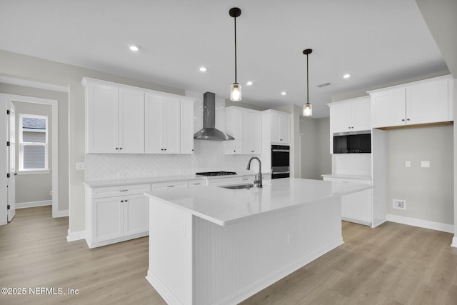 kitchen with a center island with sink, white cabinets, a sink, and wall chimney exhaust hood