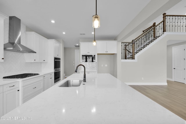 kitchen featuring light stone counters, stainless steel appliances, a sink, light wood-style floors, and wall chimney range hood