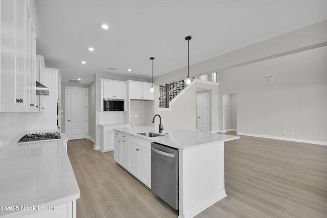 kitchen featuring a sink, light wood finished floors, stainless steel dishwasher, and an island with sink