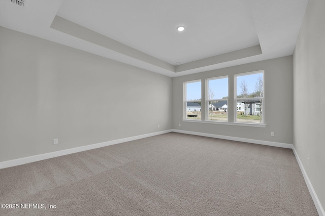 carpeted spare room with a raised ceiling and baseboards