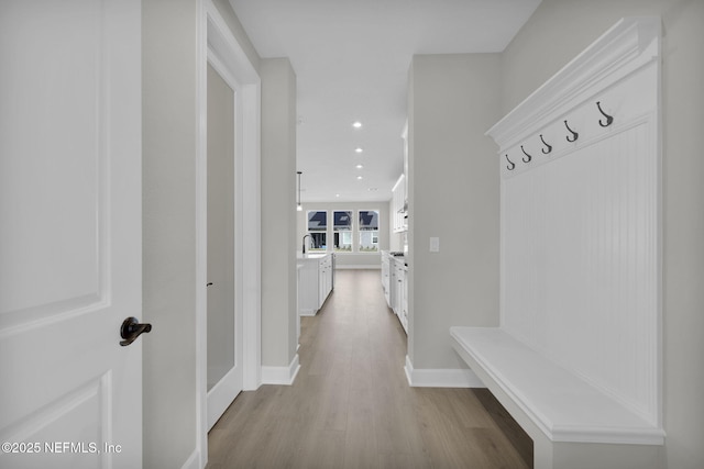 mudroom featuring recessed lighting, a sink, light wood-style flooring, and baseboards