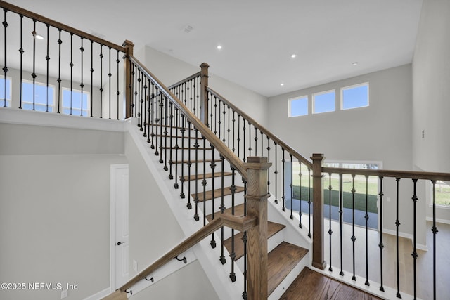 staircase featuring recessed lighting, baseboards, a high ceiling, and wood finished floors