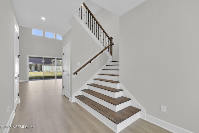 stairway featuring a high ceiling, baseboards, a wealth of natural light, and wood finished floors