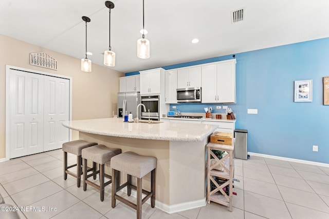 kitchen featuring stainless steel appliances, a center island with sink, white cabinets, a breakfast bar area, and decorative light fixtures