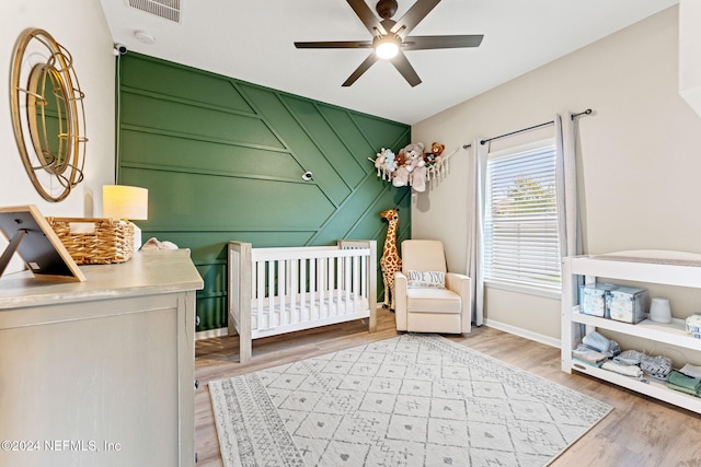 bedroom with ceiling fan, light wood-type flooring, and a nursery area