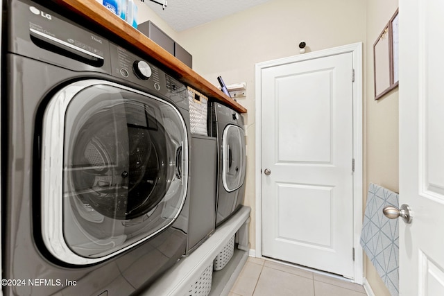 clothes washing area with a textured ceiling, light tile patterned floors, and washing machine and clothes dryer