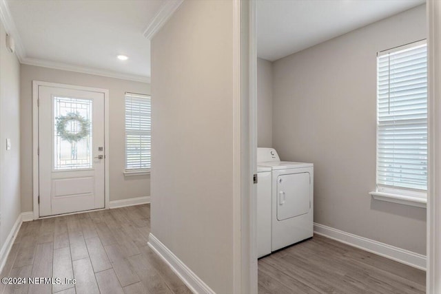 clothes washing area with light wood-type flooring, crown molding, and washer and dryer