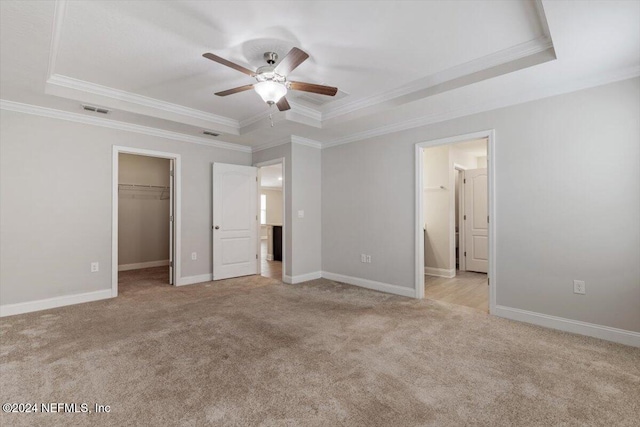 unfurnished bedroom with a walk in closet, ceiling fan, and a tray ceiling