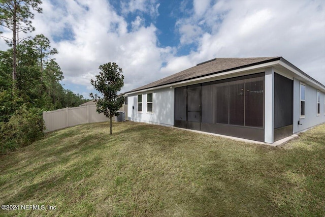 back of property featuring central air condition unit, a sunroom, and a lawn