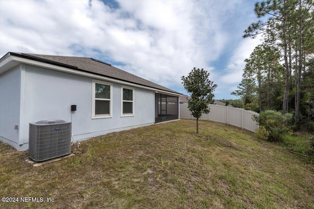 rear view of property featuring central AC unit, a sunroom, and a lawn