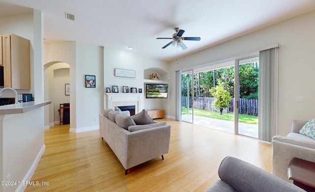 living room with ceiling fan, sink, light wood-type flooring, and built in shelves