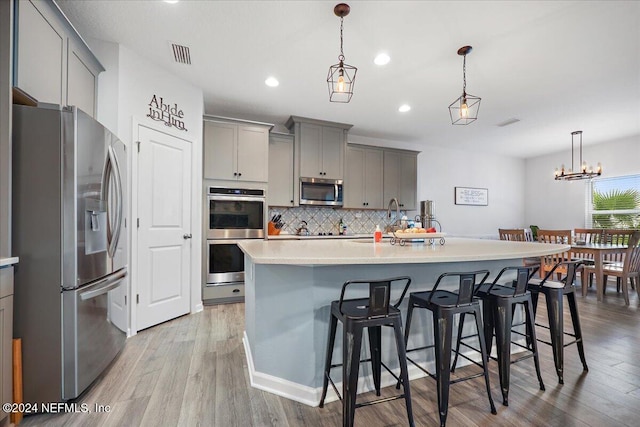 kitchen with an island with sink, gray cabinets, light wood-type flooring, and stainless steel appliances