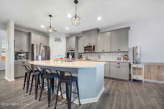 kitchen featuring a kitchen bar, pendant lighting, a kitchen island with sink, dark hardwood / wood-style flooring, and stainless steel appliances