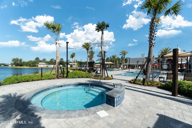 view of swimming pool with a patio area, a water view, and a hot tub