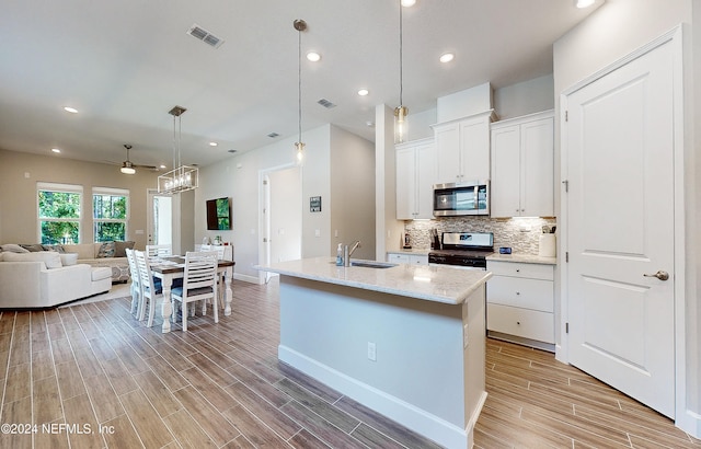 kitchen with white cabinets, light hardwood / wood-style flooring, sink, a kitchen island with sink, and appliances with stainless steel finishes