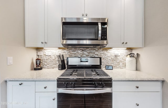 kitchen with stainless steel appliances, light stone countertops, white cabinets, and tasteful backsplash