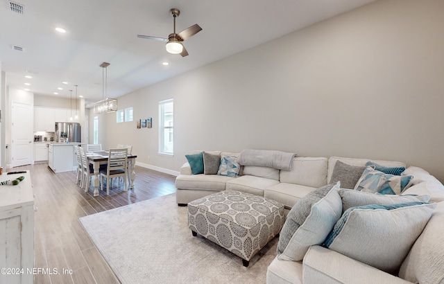 living room featuring ceiling fan with notable chandelier and light wood-type flooring