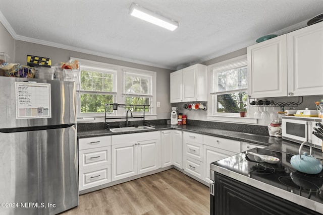 kitchen featuring sink, ornamental molding, white cabinetry, light wood-type flooring, and stainless steel fridge