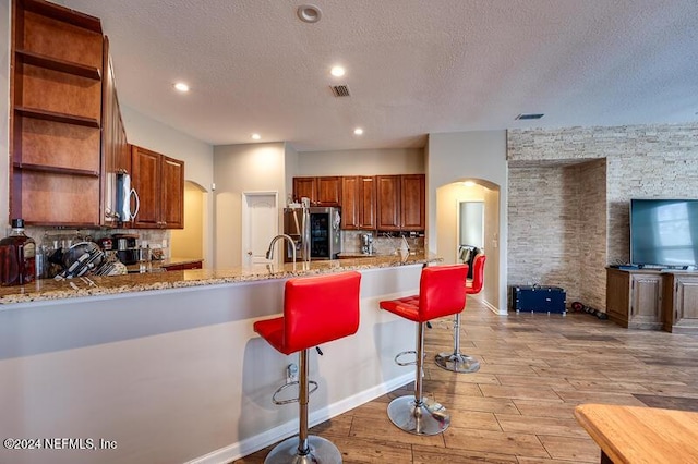 kitchen featuring light stone countertops, appliances with stainless steel finishes, a kitchen bar, and kitchen peninsula