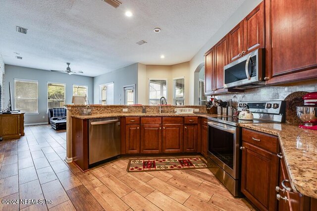 kitchen with stainless steel appliances, sink, light hardwood / wood-style floors, and kitchen peninsula