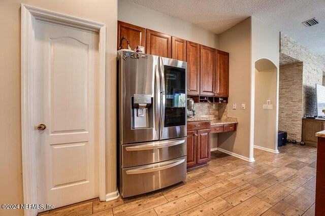 kitchen with light hardwood / wood-style flooring, backsplash, stainless steel refrigerator with ice dispenser, light stone counters, and a textured ceiling